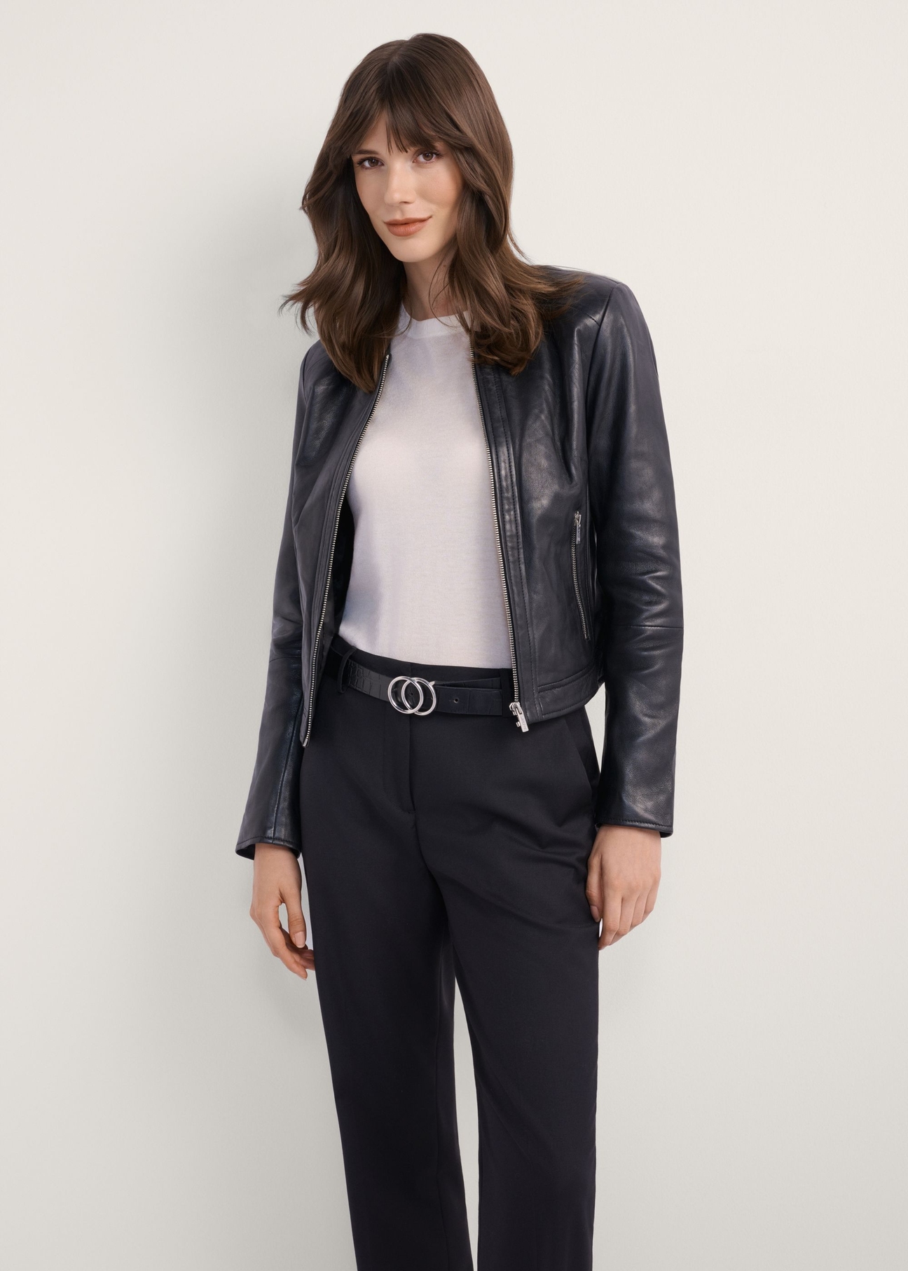 Жіноча чорна коротка шкіряна куртка KURDS-0294-99(KS), вигляд виробу спереду на моделі. Видно половину силуету.