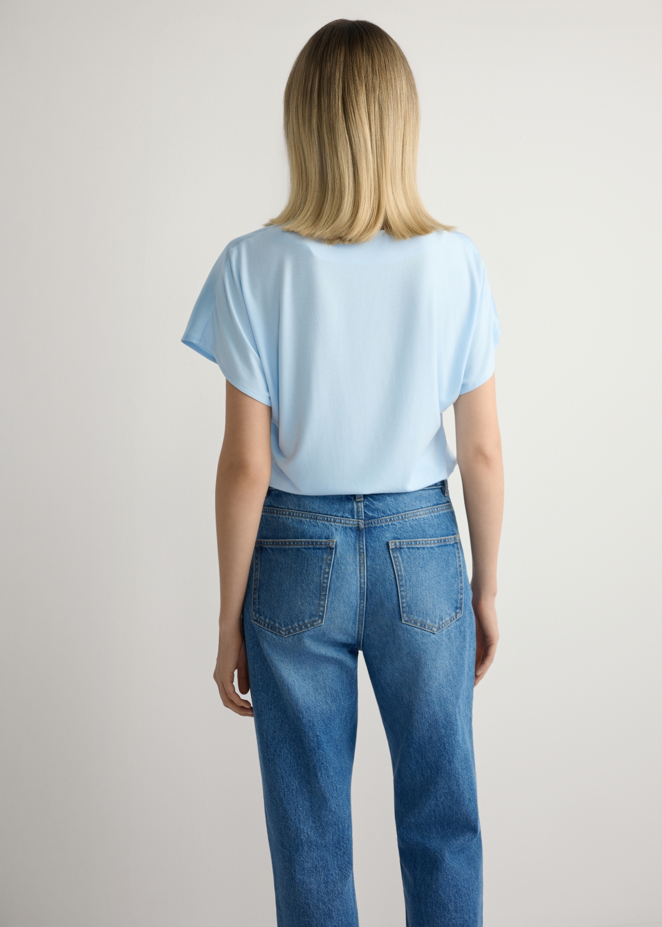 Світло-блакитна жіноча блузка BLUDT-0206-7A(W26), вигляд виробу ззаду на моделі. Видно половину силуету.