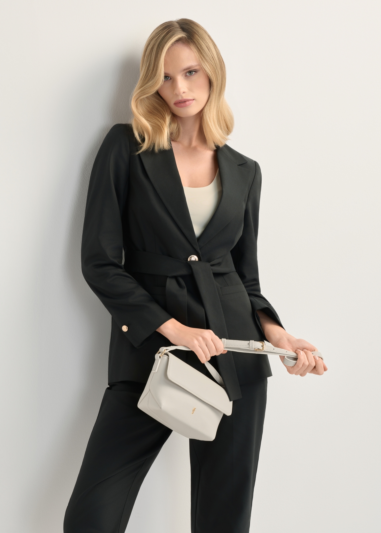 Кремова маленька жіноча сумка через плече TOREC-0916-0B(W26), вигляд виробу спереду в руці моделі. Видно половину силуету.