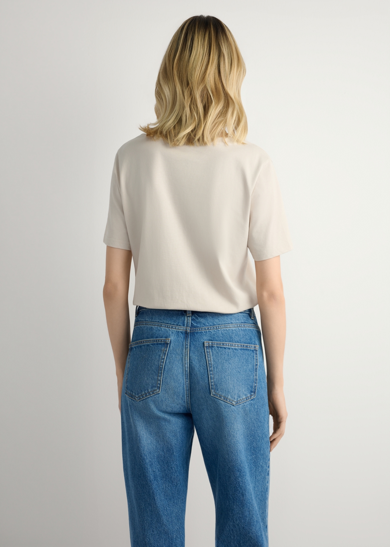 Світло-бежева жіноча базова футболка TSHDT-0120-1A(W26), вигляд виробу ззаду на моделі. Видно половину силуету.