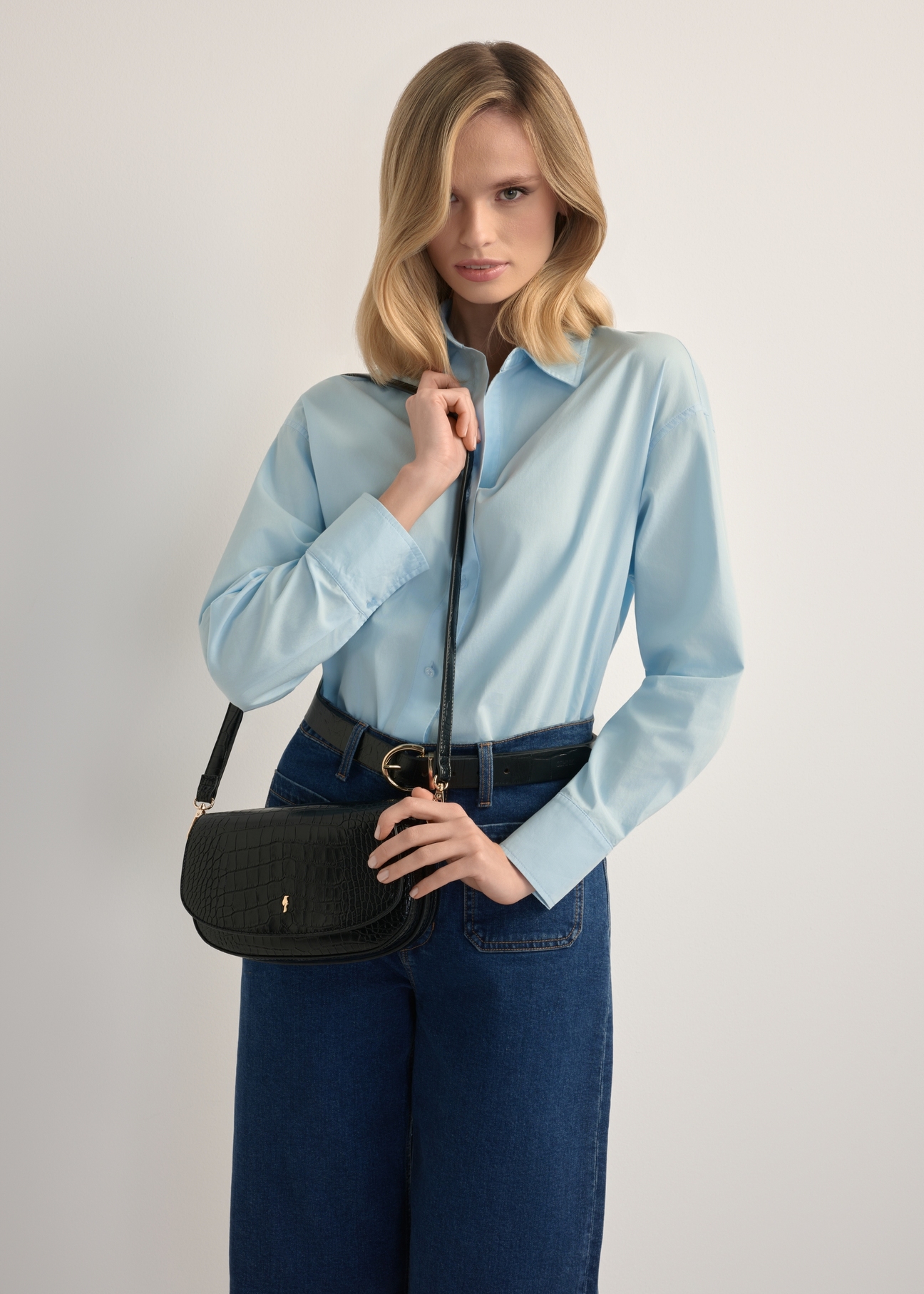 Маленька чорна жіноча сумка-месенджер з крокоподібної шкіри TOREC-1185-9G(W26), вигляд виробу на плечі моделі. Видно половину силуету.