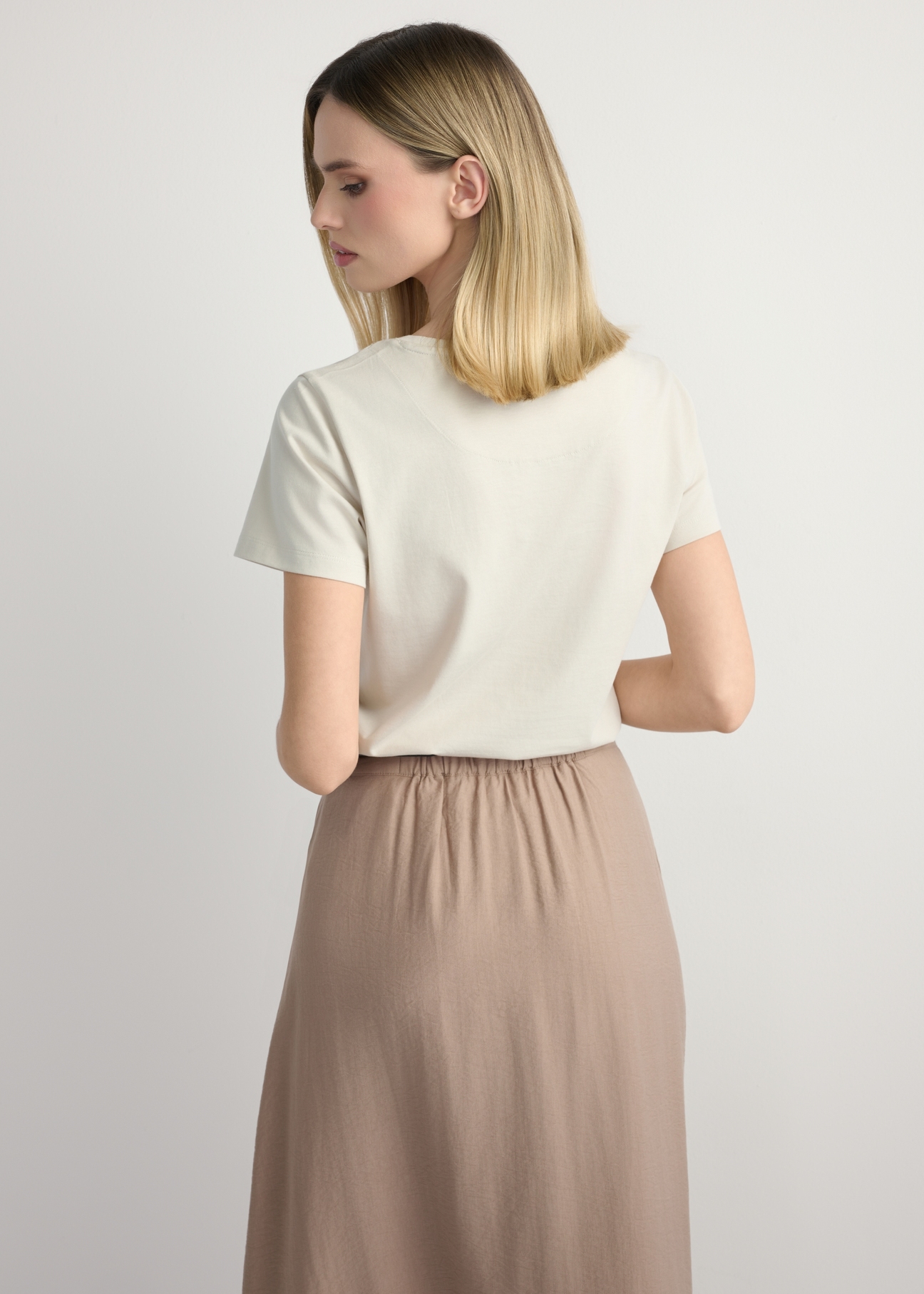 Світло-бежева жіноча футболка з логотипом TSHDT-0157-1A(W26), вигляд виробу ззаду на моделі. Видно половину силуету.