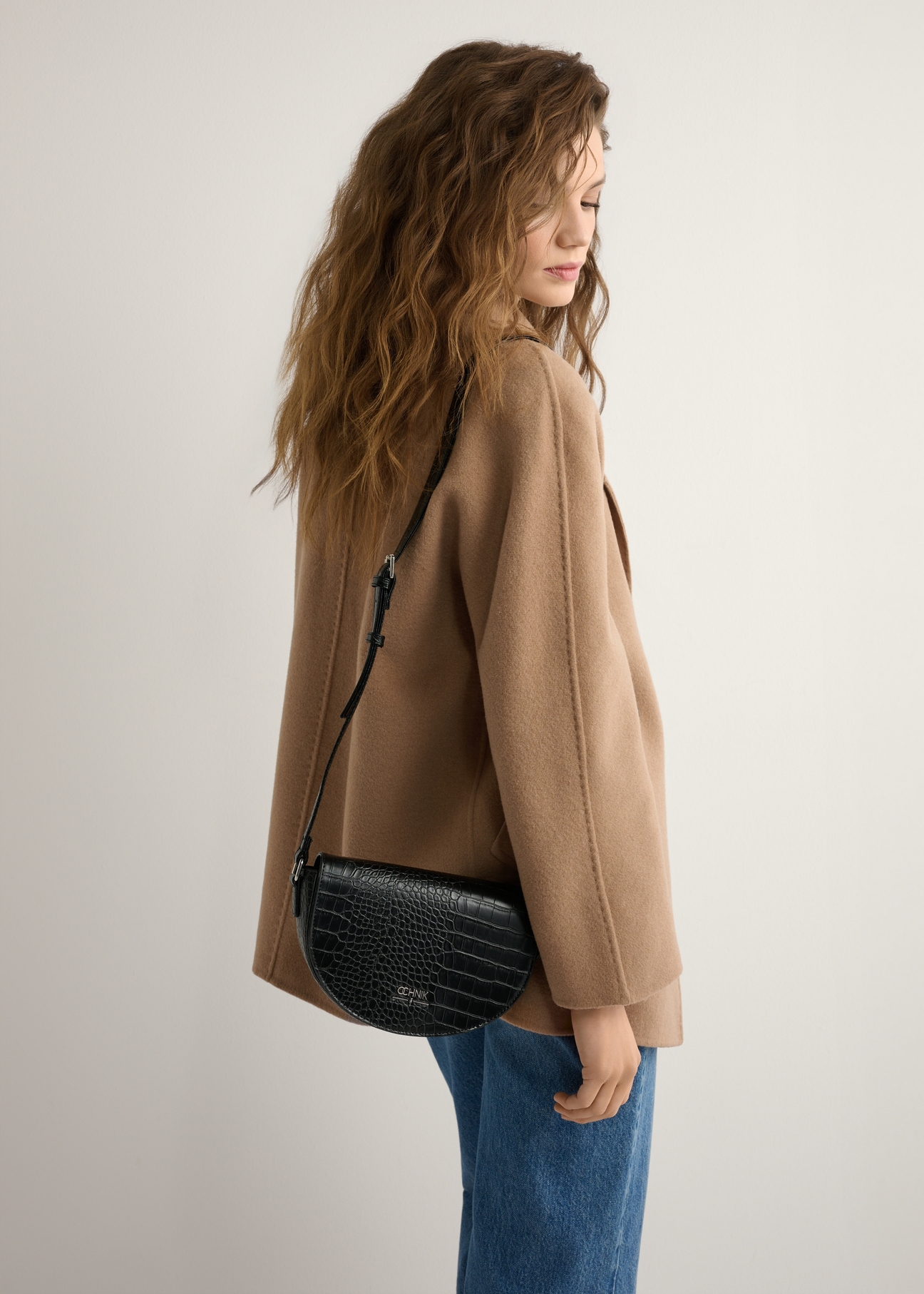 Жіноча чорна напівкругла сумка-месенджер з крокодилової шкіри TOREC-1184-9G(W26), вигляд виробу на плечі моделі. Видно половину силуету.