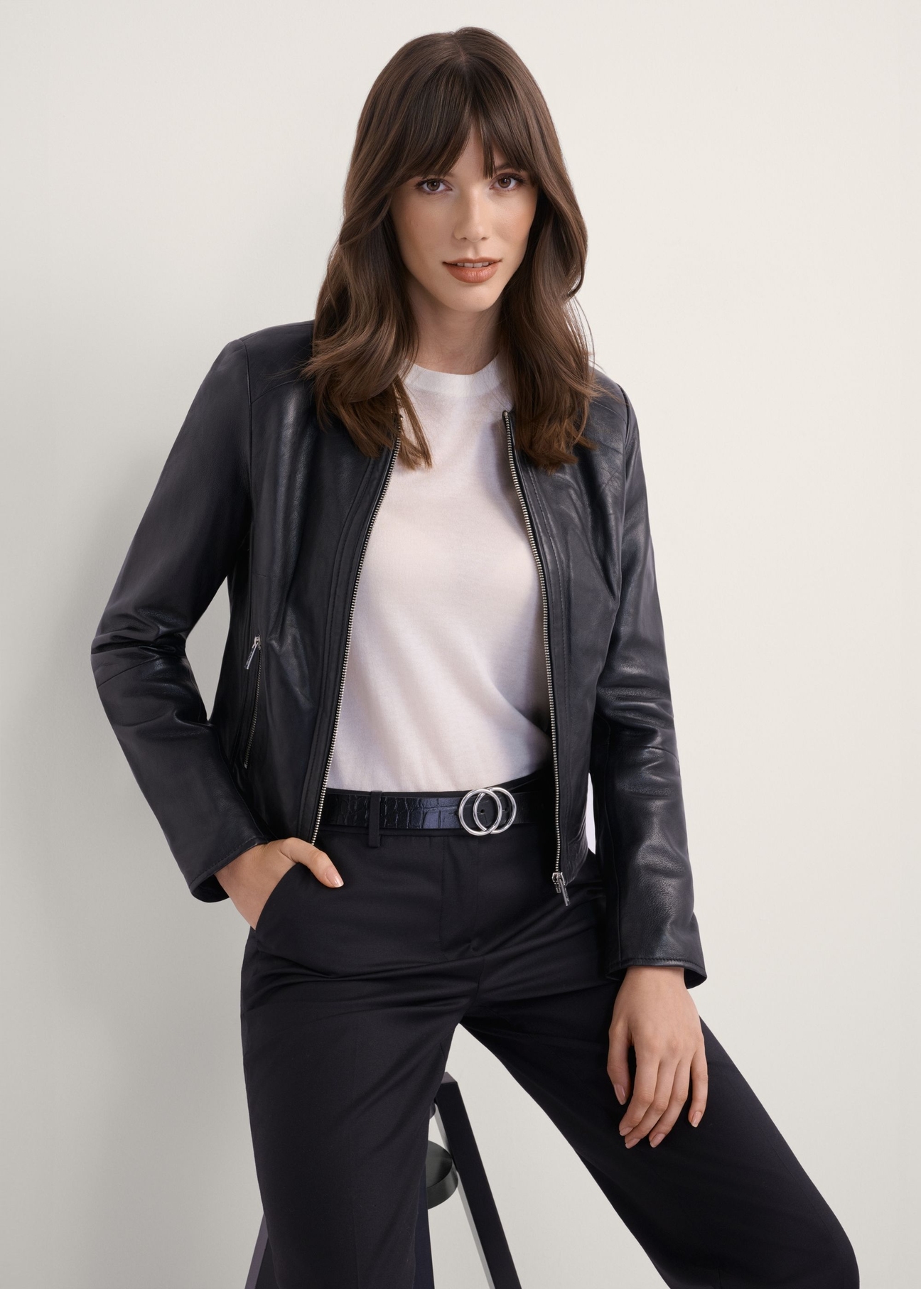 Жіноча чорна коротка шкіряна куртка KURDS-0294-99(KS), вигляд виробу спереду на моделі. Видно половину силуету.