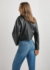 Жіноча коротка шкіряна куртка чорного кольору KURDS-0597-99(W26), вигляд виробу ззаду на моделі. Видно половину силуету.